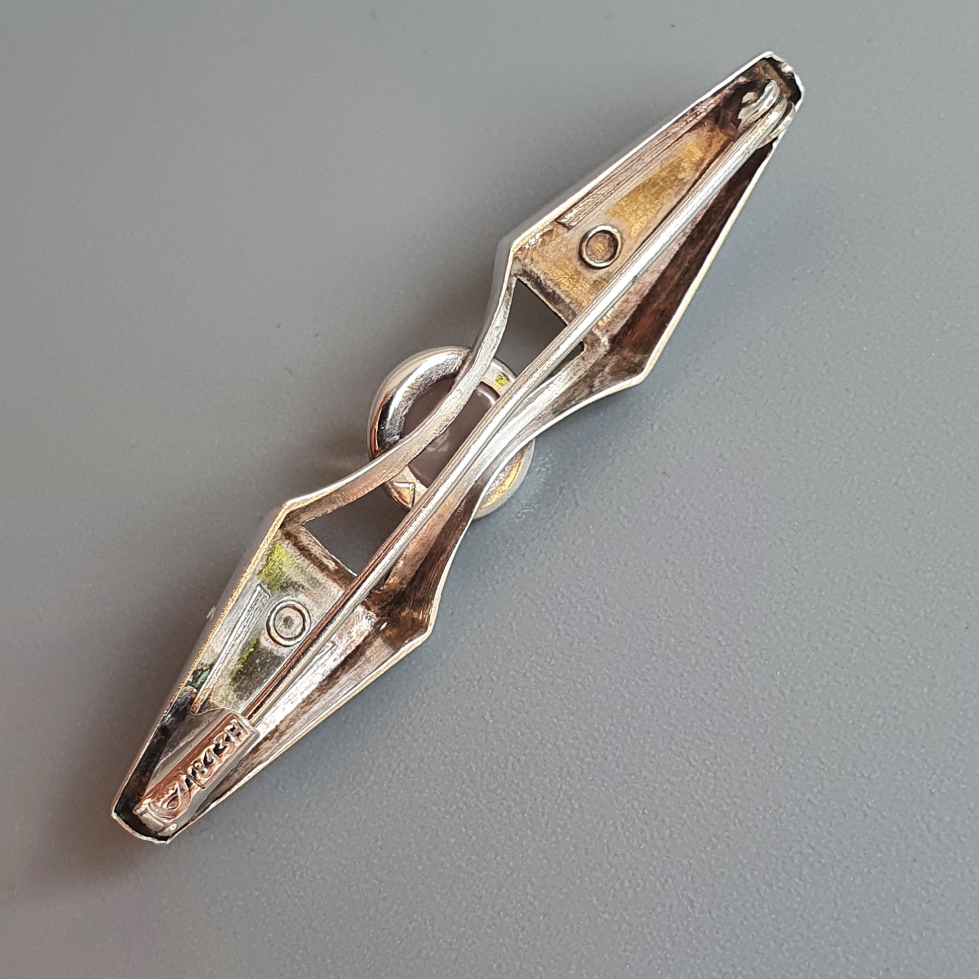 Metal clamp or clip with a diamond-shaped body and pointed ends.