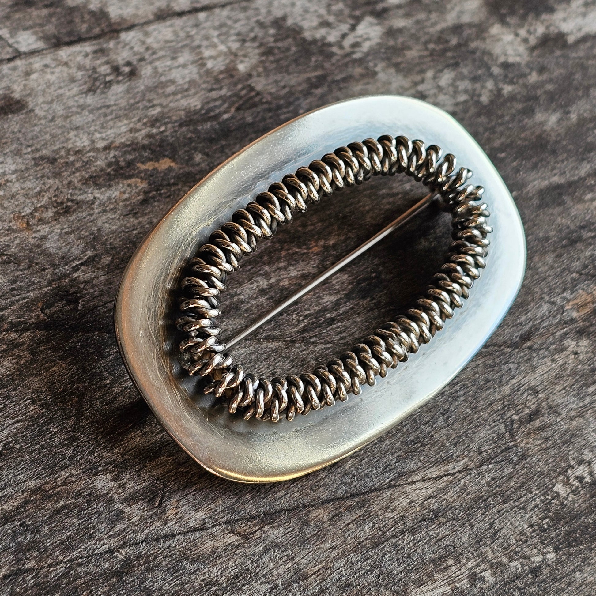 Oval-shaped brooch or pin with a metallic coiled wire design in the center.