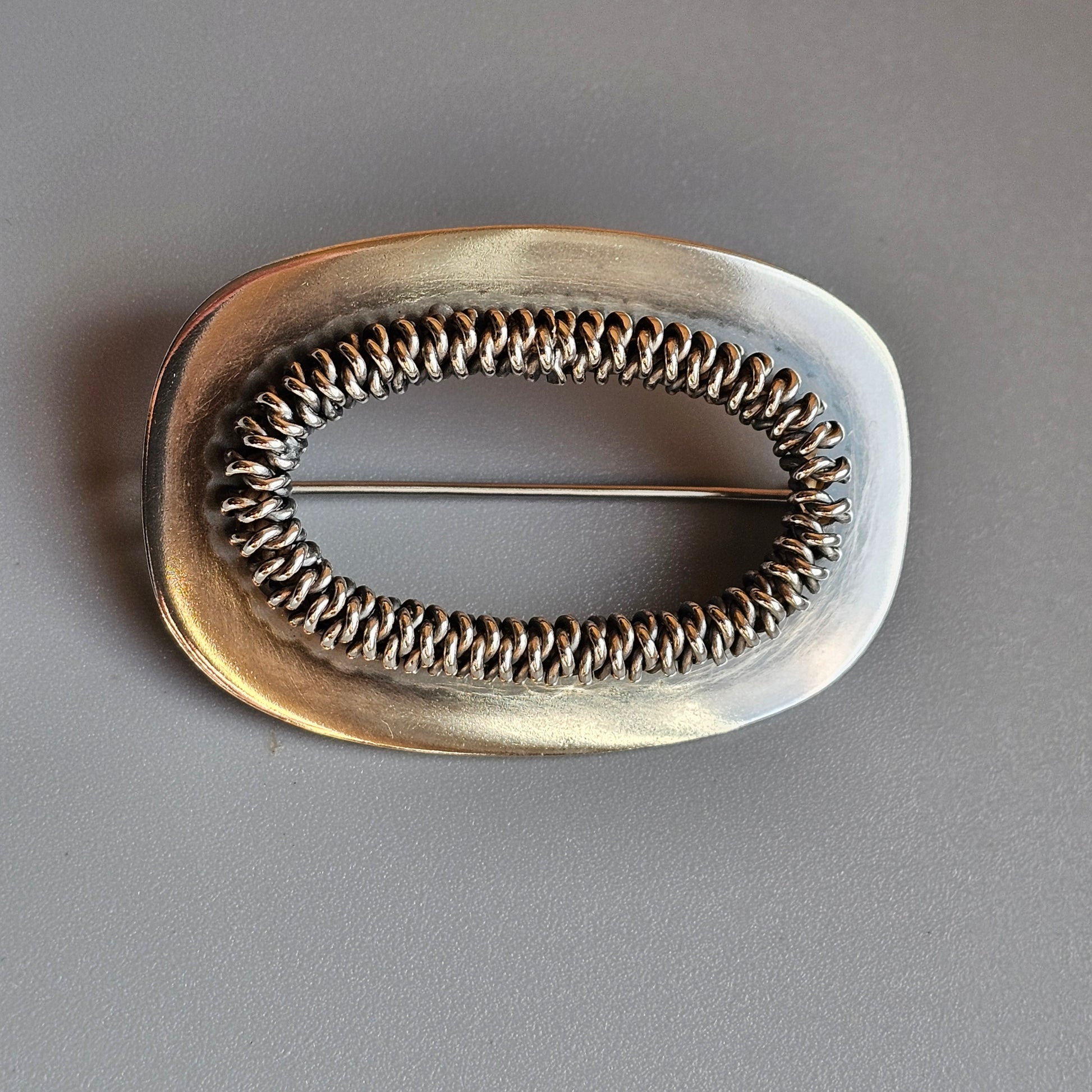 Oval-shaped silver brooch with intricate wire-wrapped interior design.