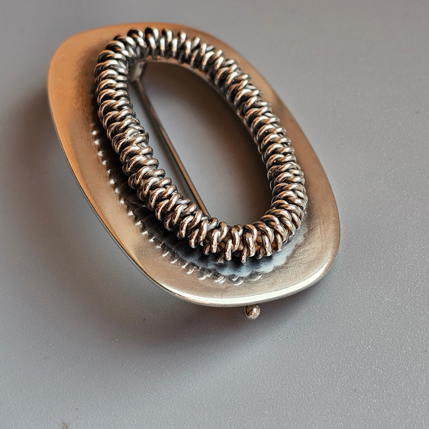 Oval-shaped hair tie or scrunchie with a metallic coiled design.