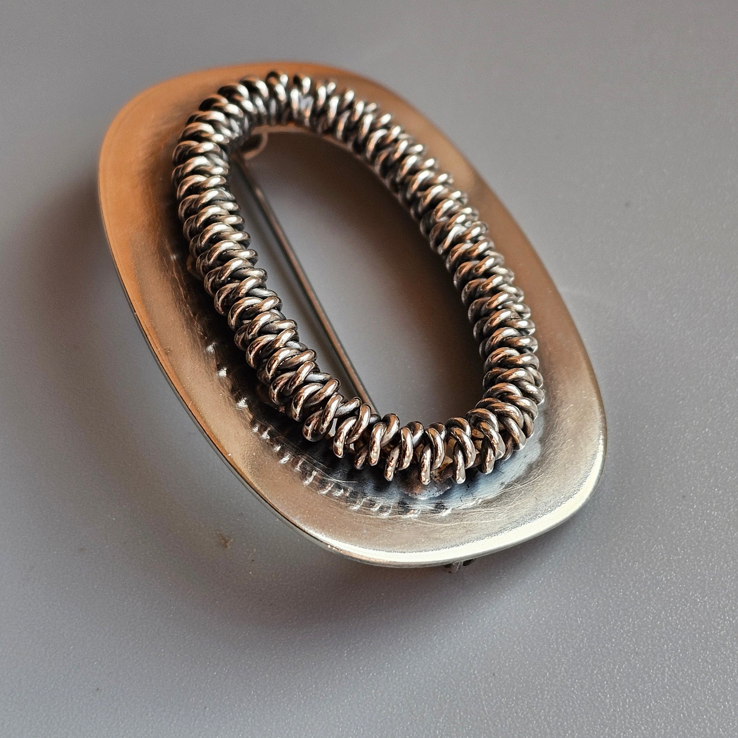 Oval-shaped metal hair tie or elastic with a coiled spring-like design.