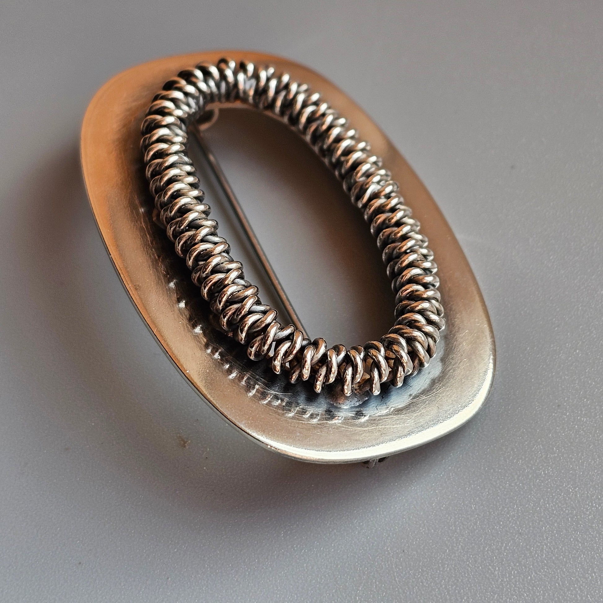 Oval-shaped metal hair tie or elastic with a coiled spring-like design.