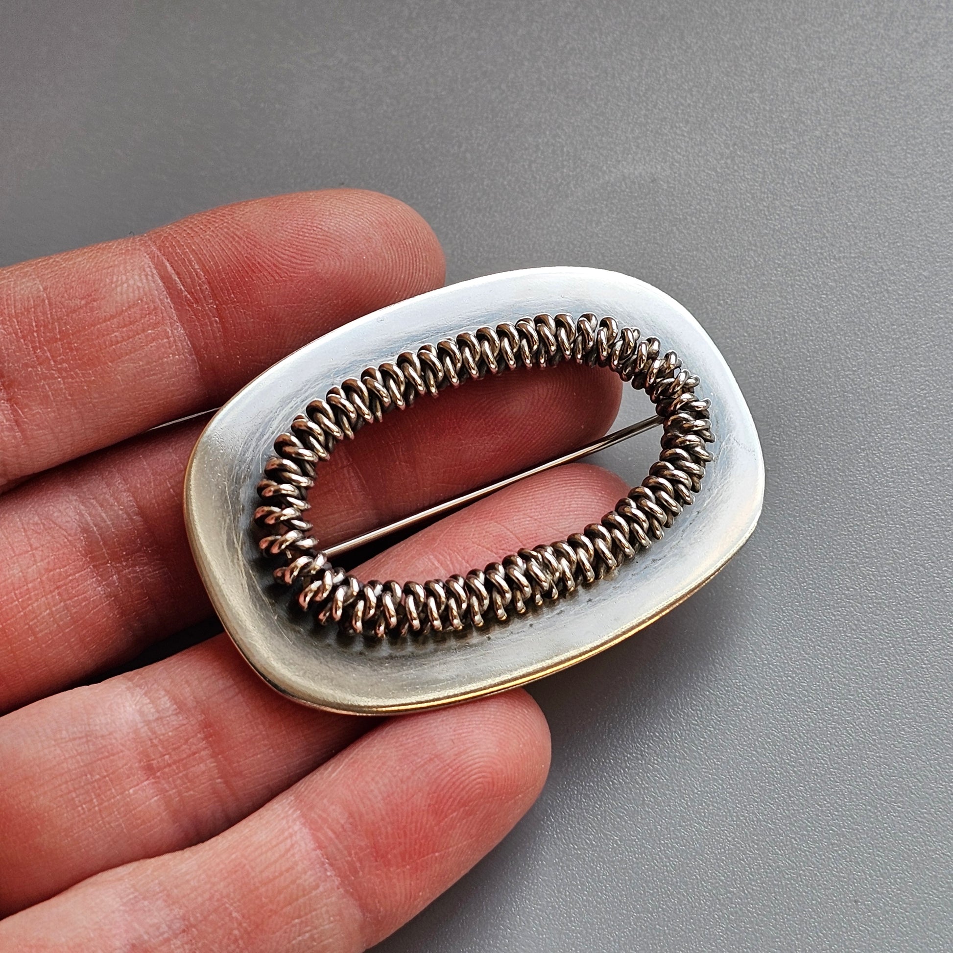 Oval-shaped silver brooch with a coiled wire design in the center.