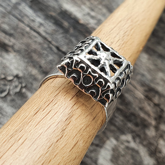 Ornate silver ring with an intricate openwork design on a wooden surface.