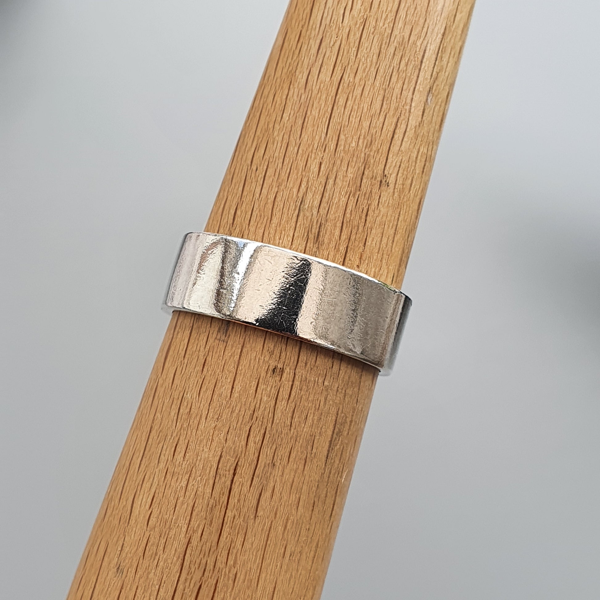 Silver ring with a hammered or textured surface displayed on a wooden surface.