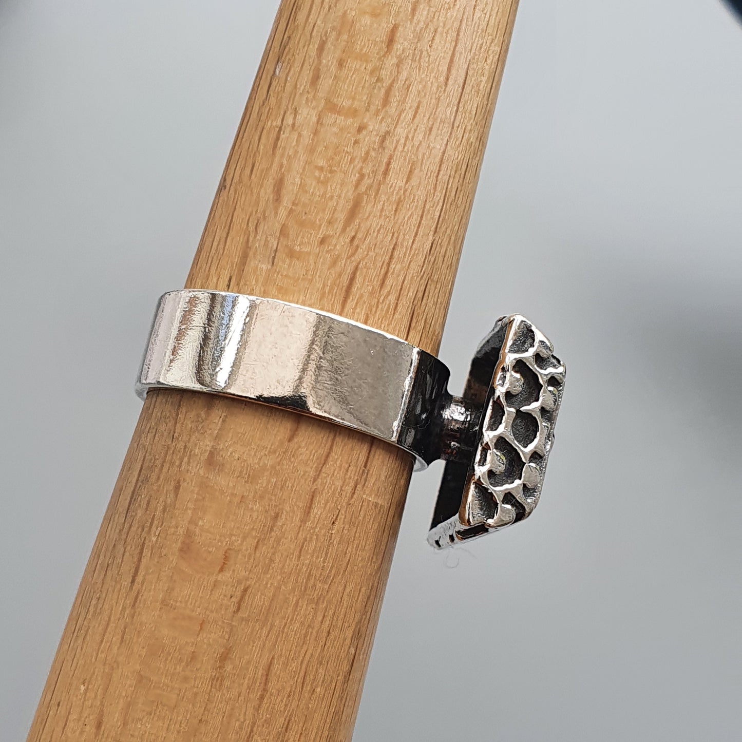 Silver ring with a decorative patterned attachment on a wooden surface.