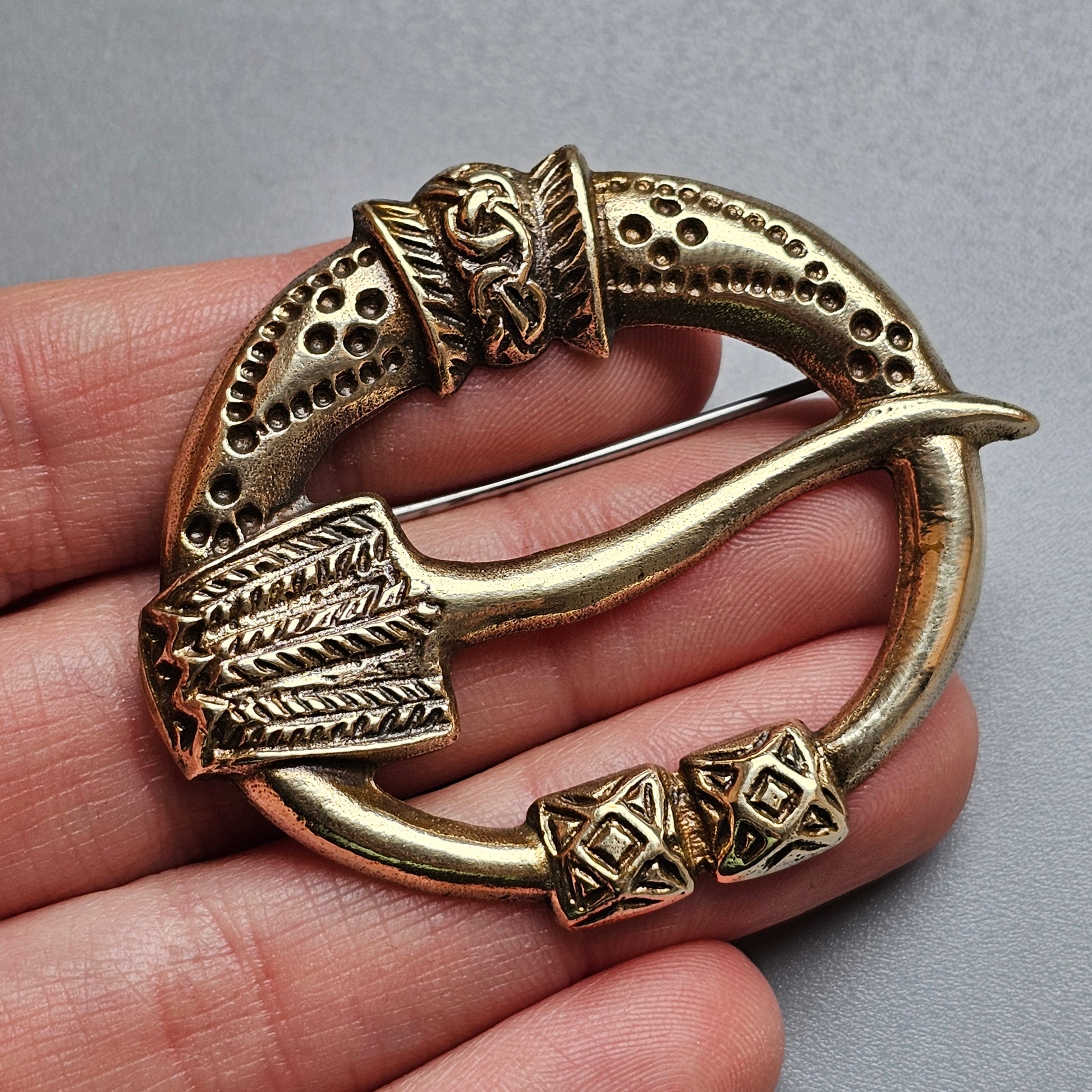 Ornate bronze or brass penannular brooch with intricate Celtic-style designs.