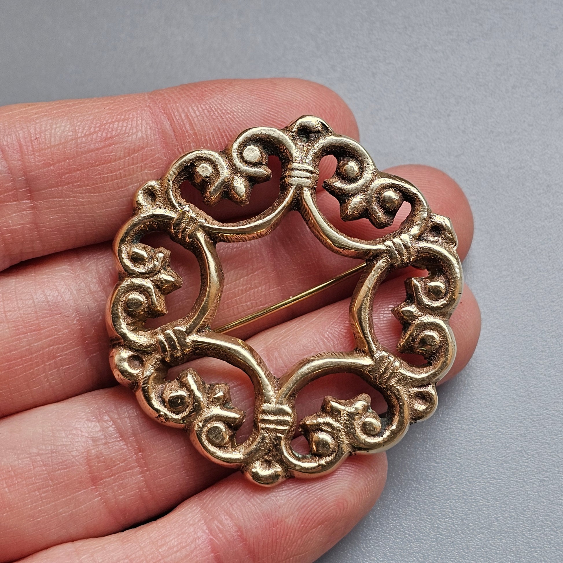 Ornate circular gold-toned brooch with intricate scrollwork design.