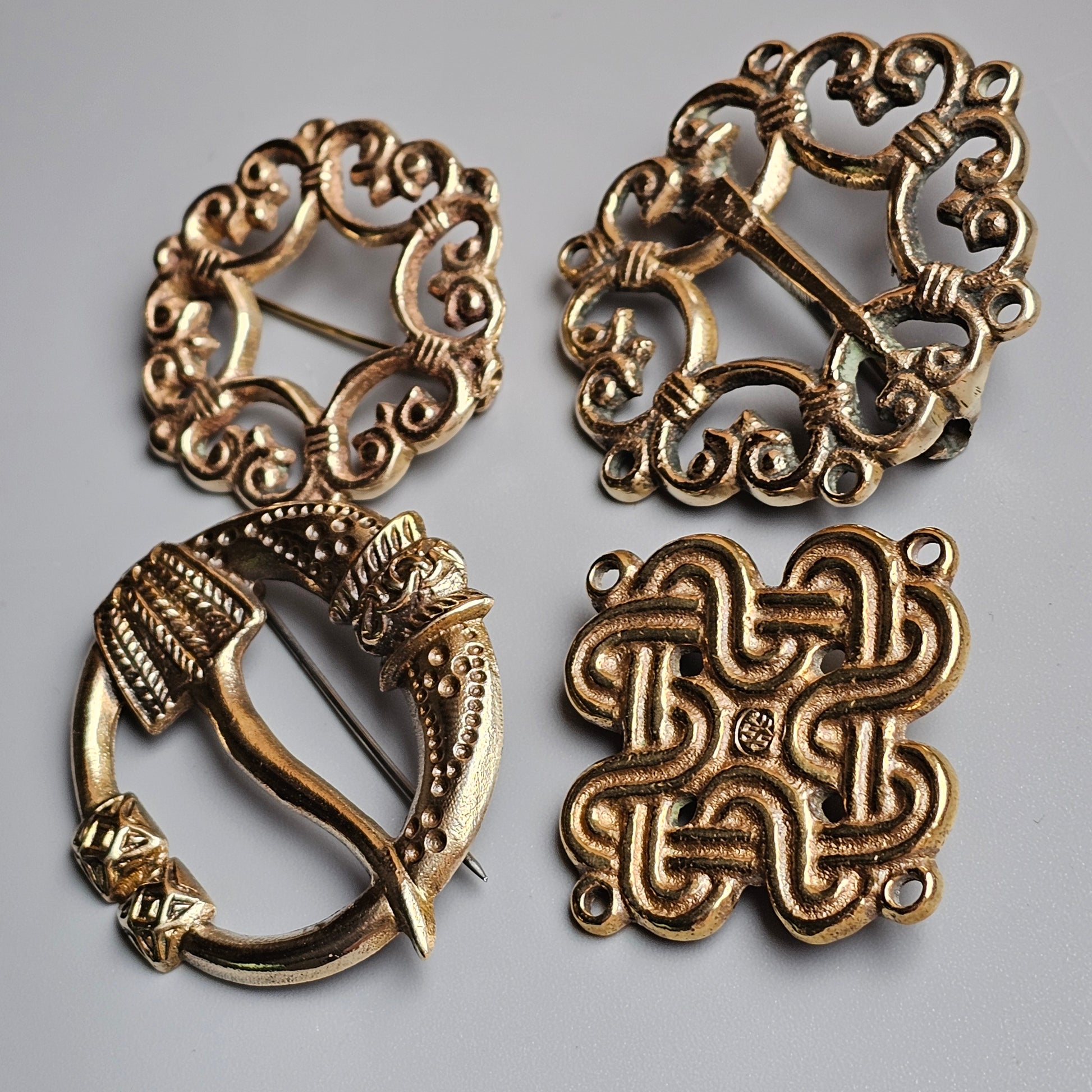 Four ornate antique bronze or brass brooches with intricate Celtic-inspired designs.