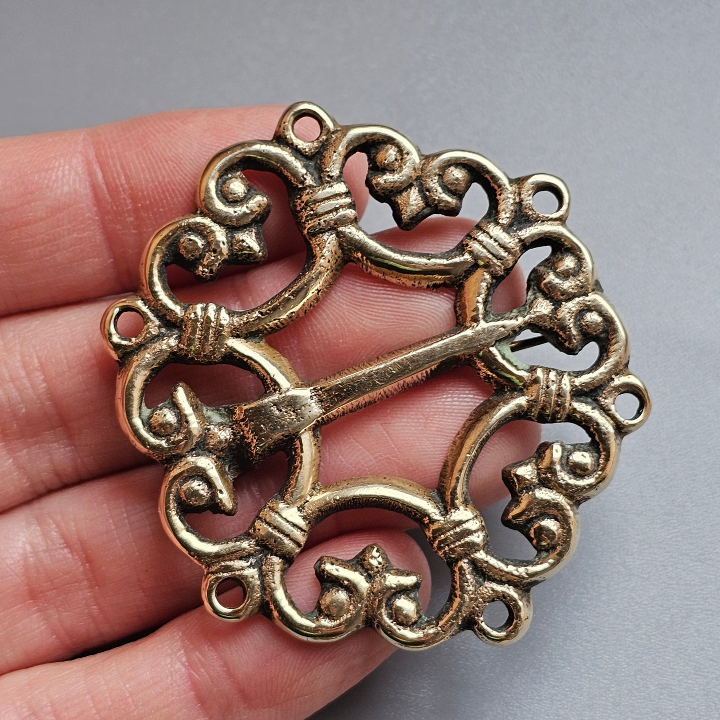 Ornate bronze or brass brooch with intricate swirling designs and a central pin.