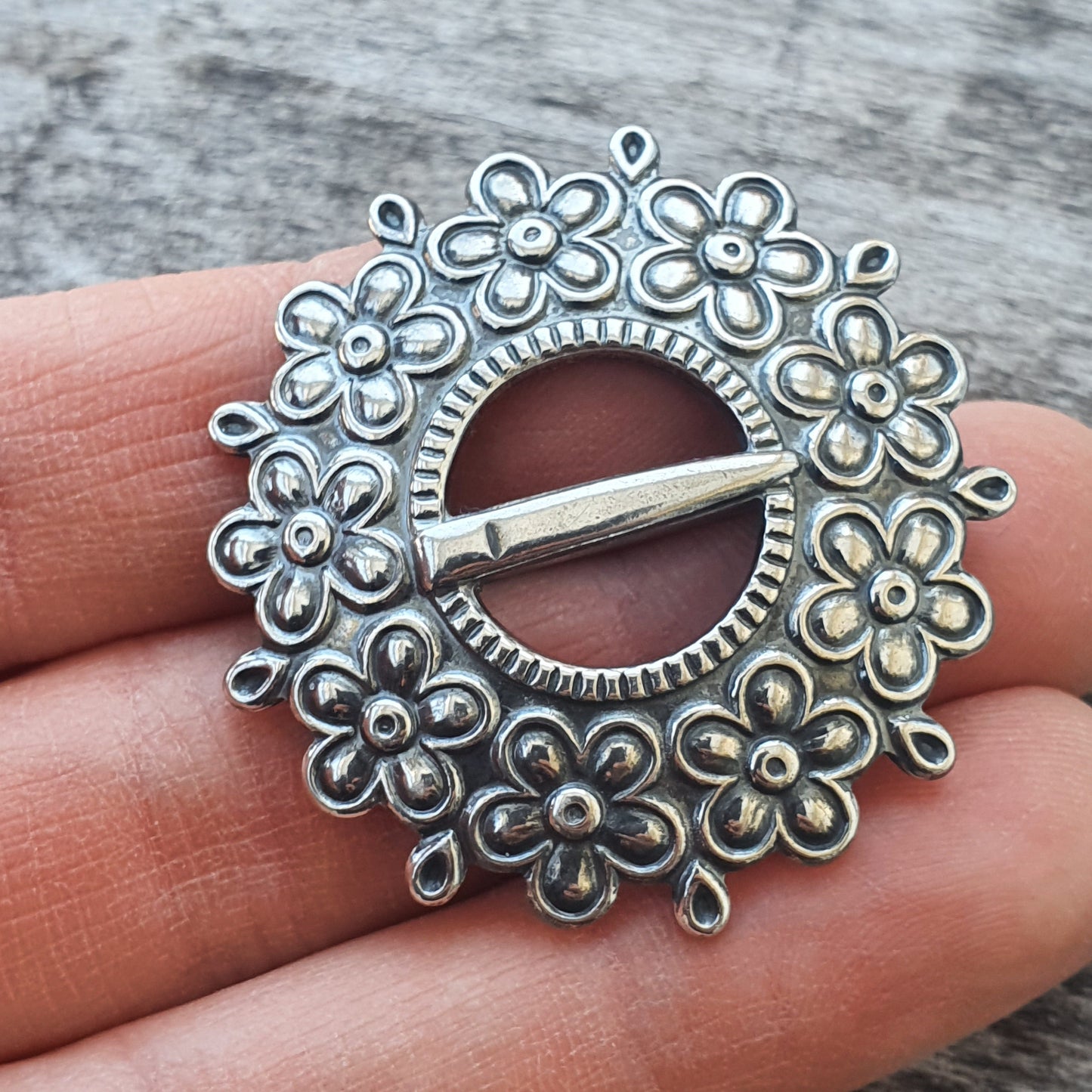 Ornate silver brooch with floral design surrounding a central pin.