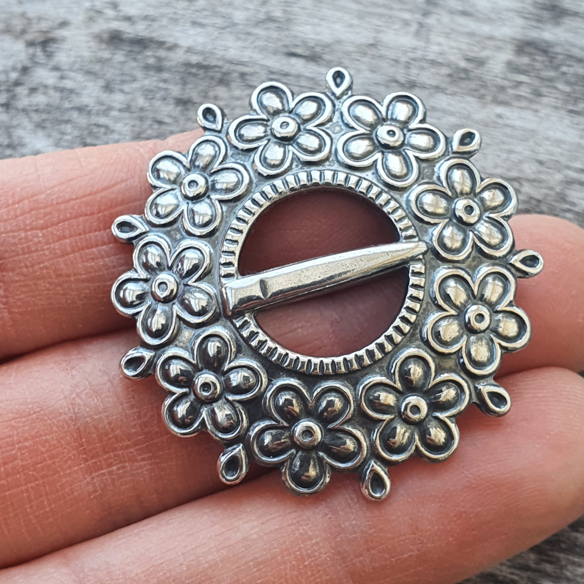 Ornate silver brooch with floral design surrounding a central pin.