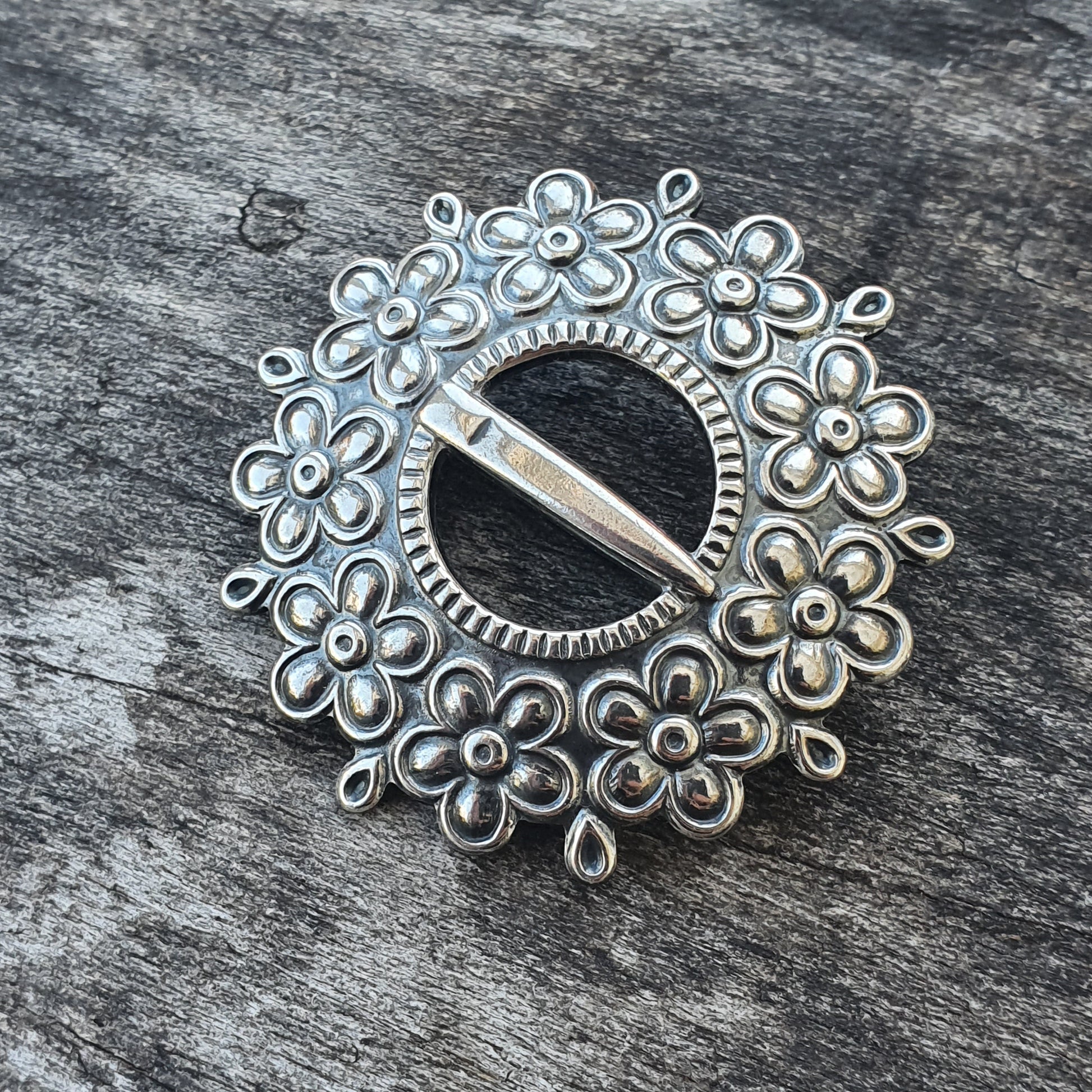 Ornate silver brooch with a circular design featuring floral patterns.