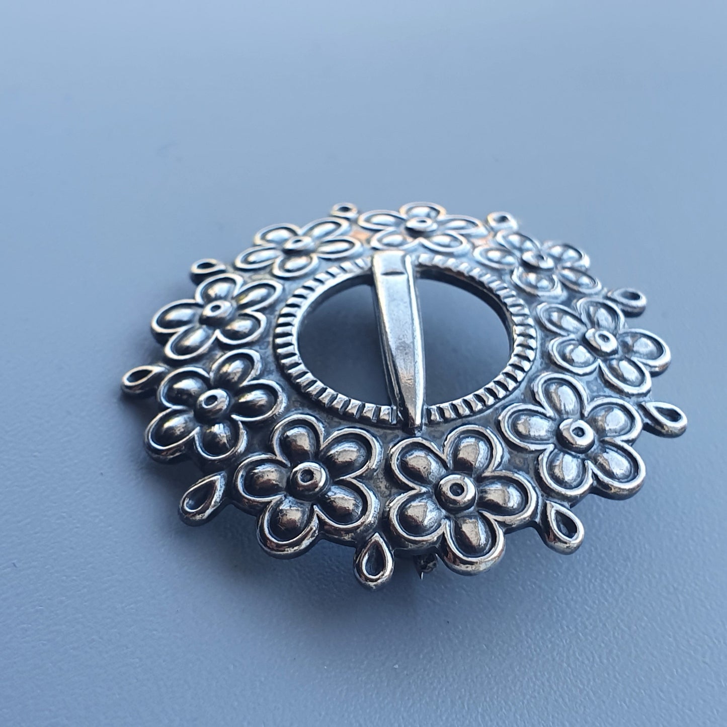 Ornate silver brooch with floral design surrounding a central circular pin.