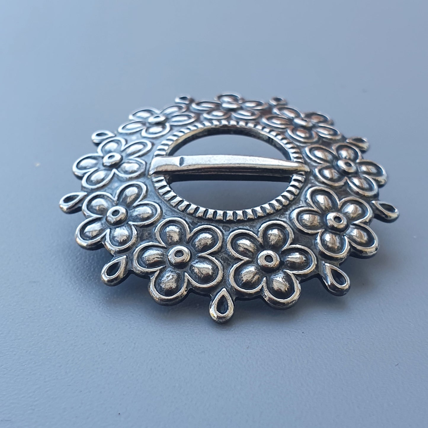 Ornate silver brooch with a floral design surrounding a central oval opening.