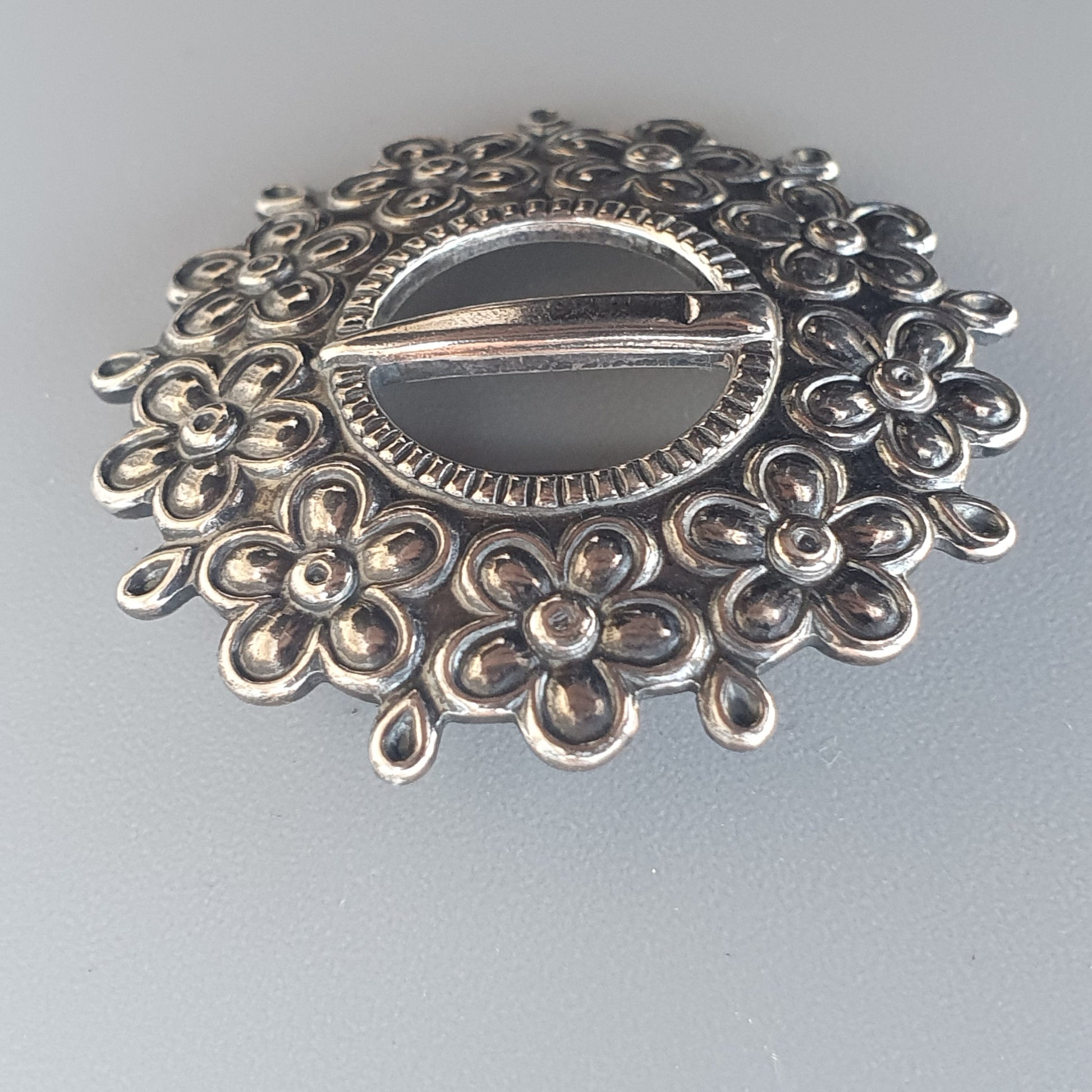 Ornate silver brooch with floral filigree design surrounding a central oval shape.