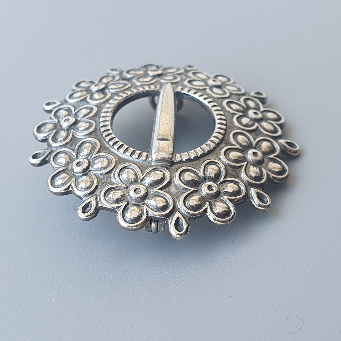 Ornate silver brooch or pin with a floral design surrounding a central circular opening.