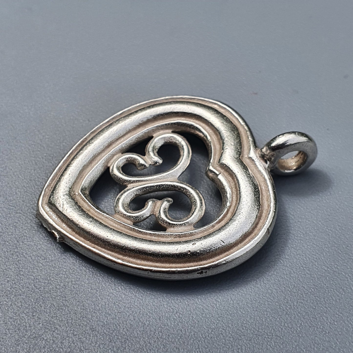 Heart-shaped silver pendant with an intricate swirl design inside.