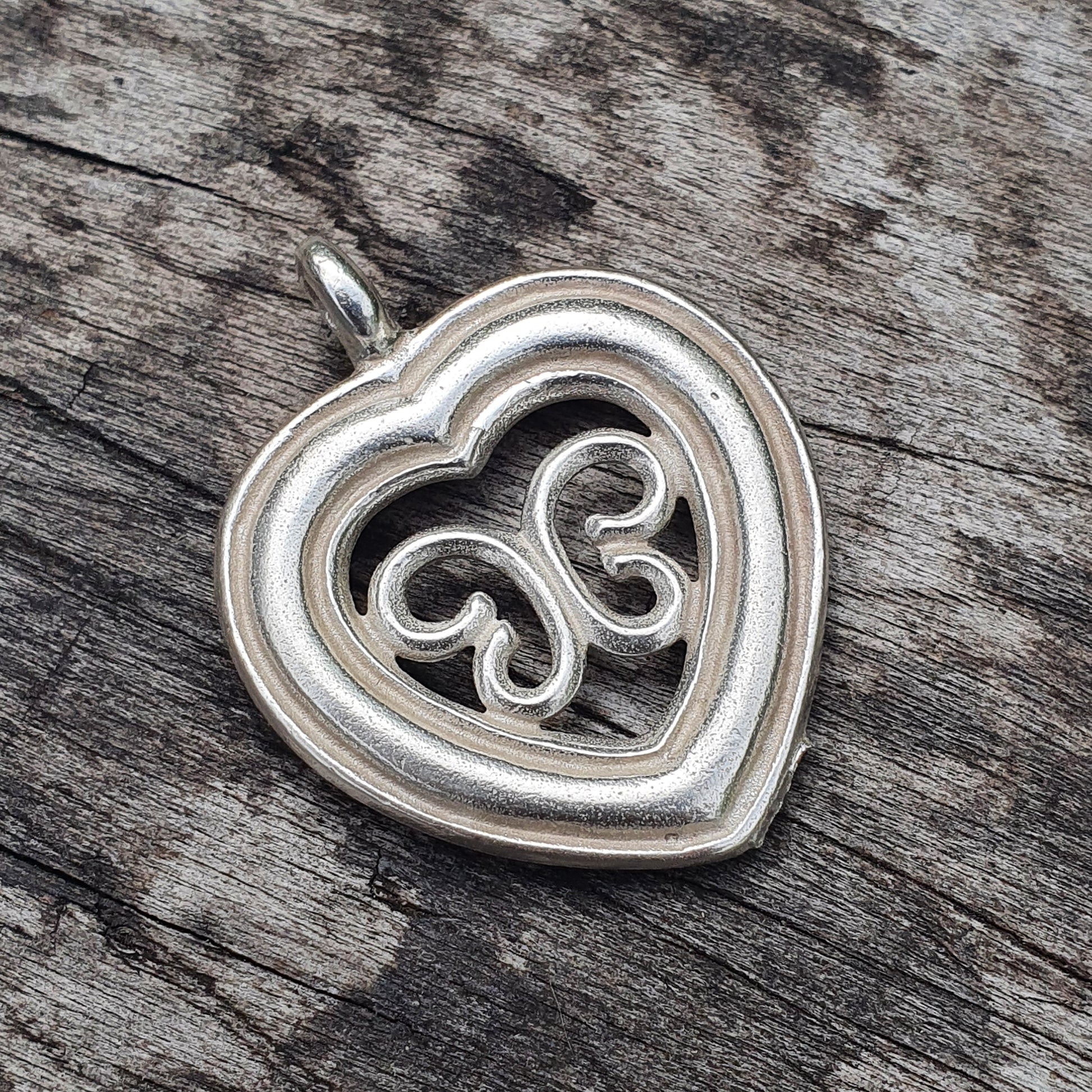 Silver heart-shaped pendant with an intricate swirl design inside.