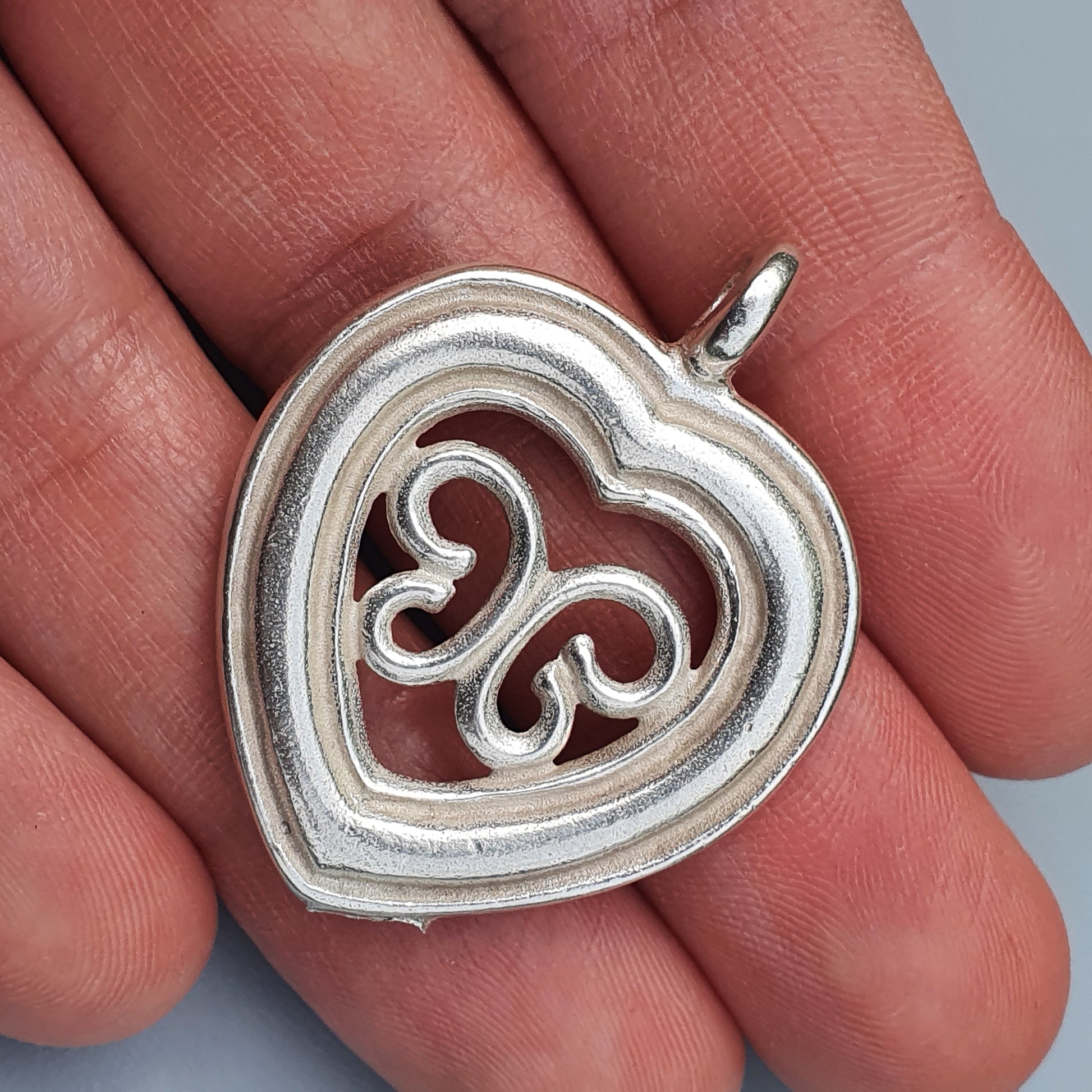 Silver heart-shaped pendant with an intricate swirl design inside.