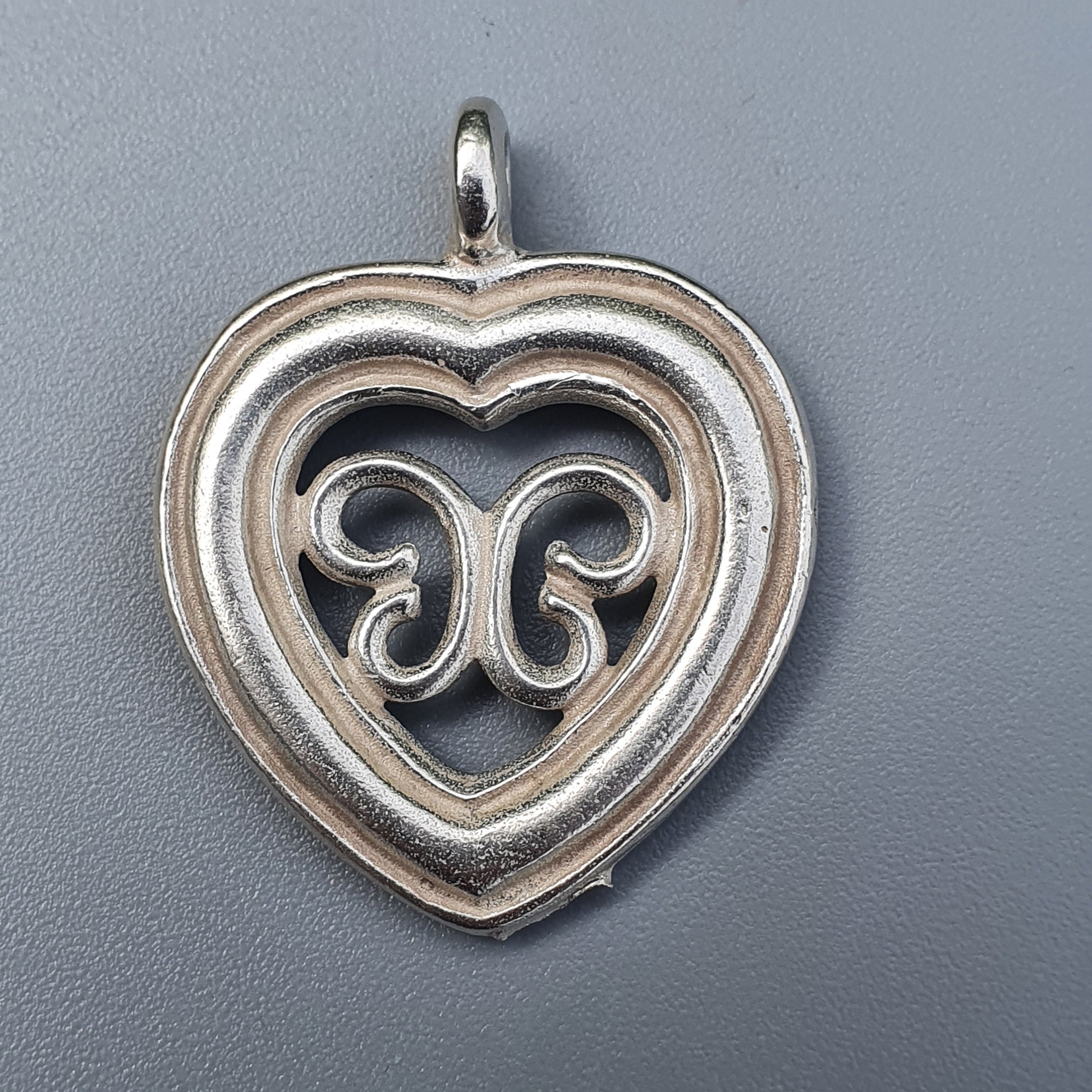 Silver heart-shaped pendant with an ornate swirl design in the center.