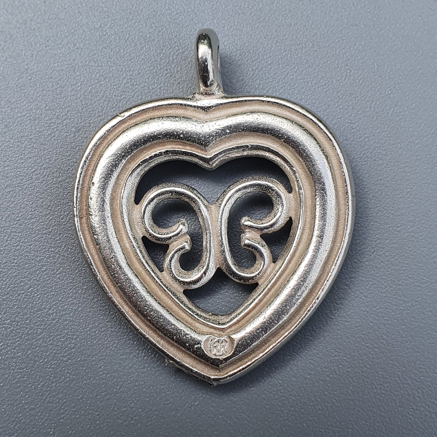 Heart-shaped silver pendant with intricate scrollwork design.