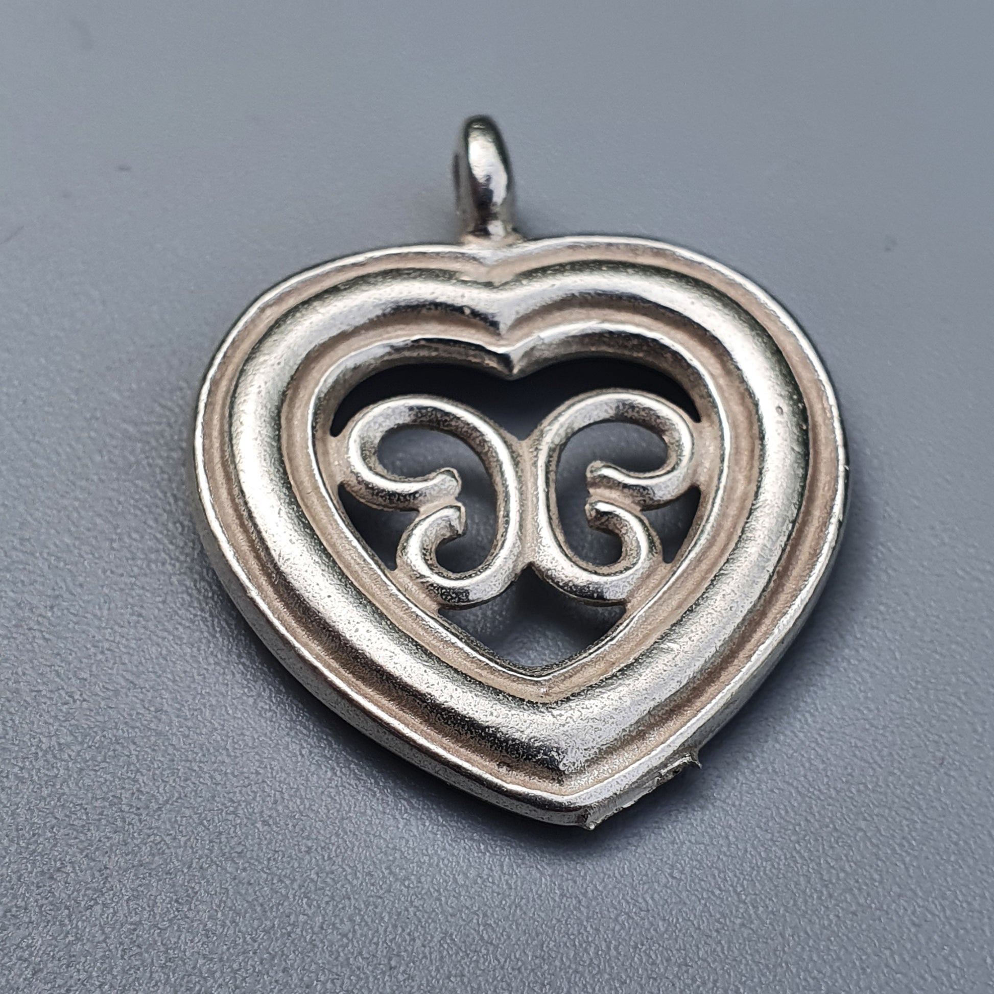 Heart-shaped silver pendant with an intricate swirl design in the center.