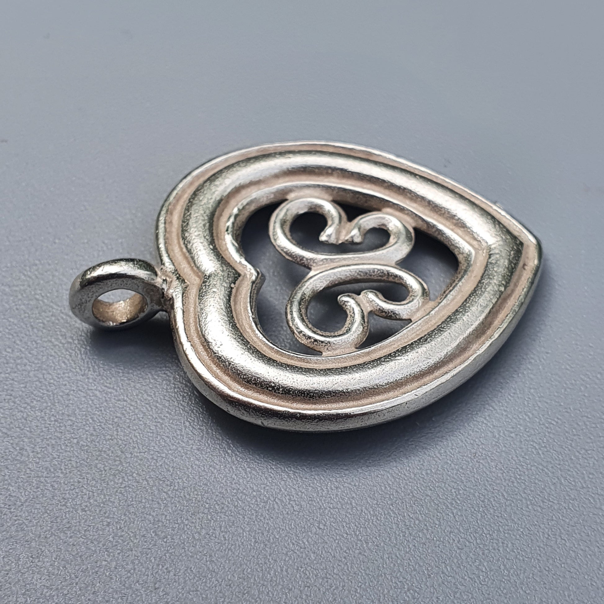 Silver heart-shaped pendant with intricate swirl designs inside.