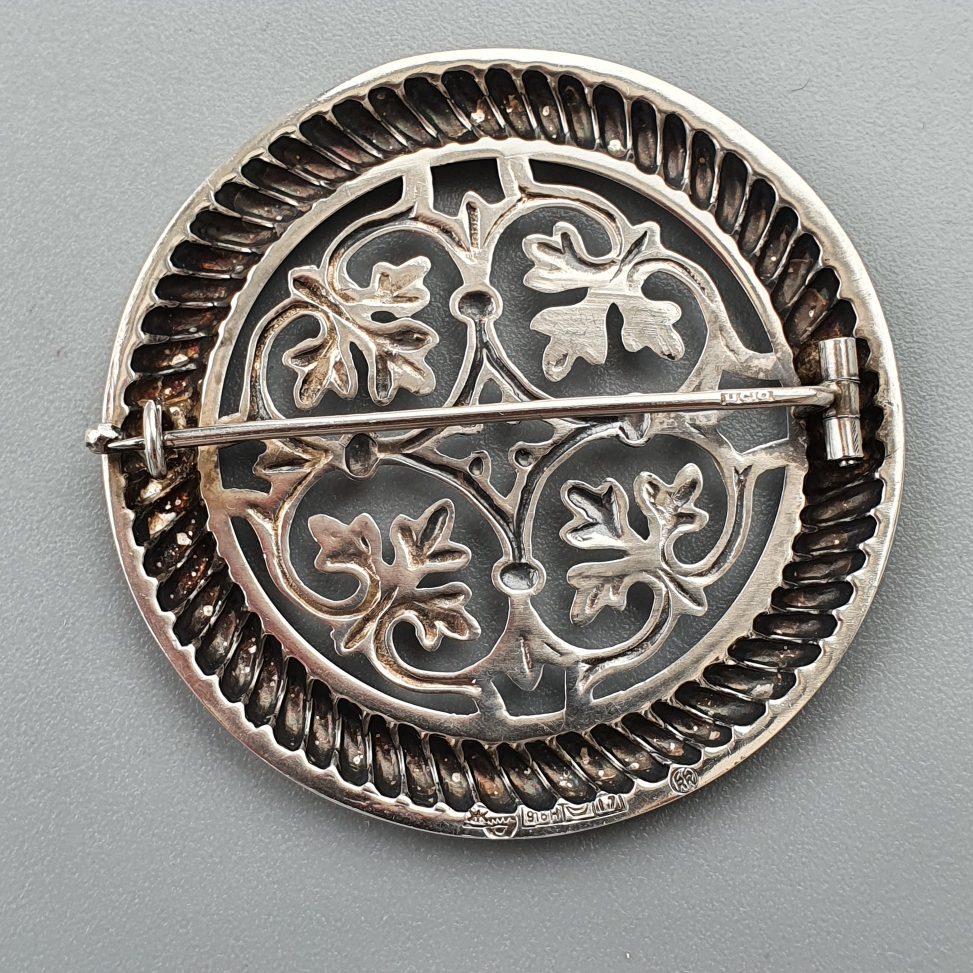 Ornate circular silver brooch with floral motifs and a pin clasp.