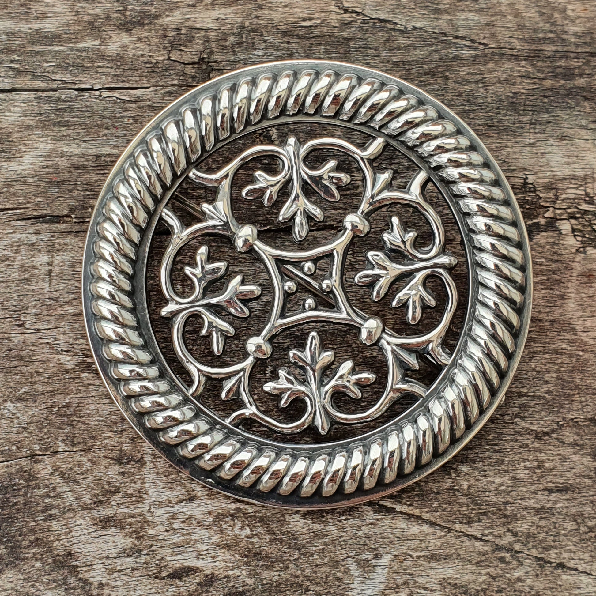 Ornate silver brooch or medallion with intricate floral scrollwork design.