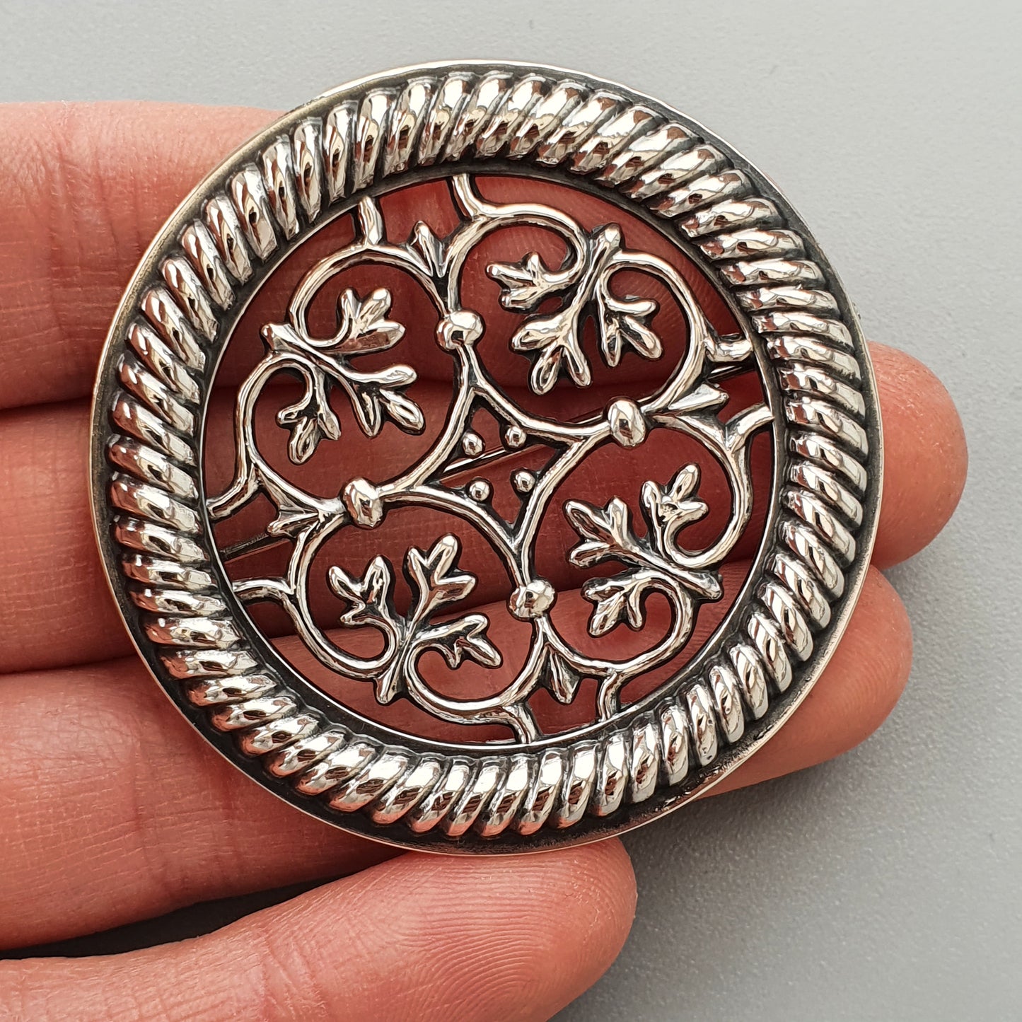 Ornate silver brooch with intricate floral design on a red background.