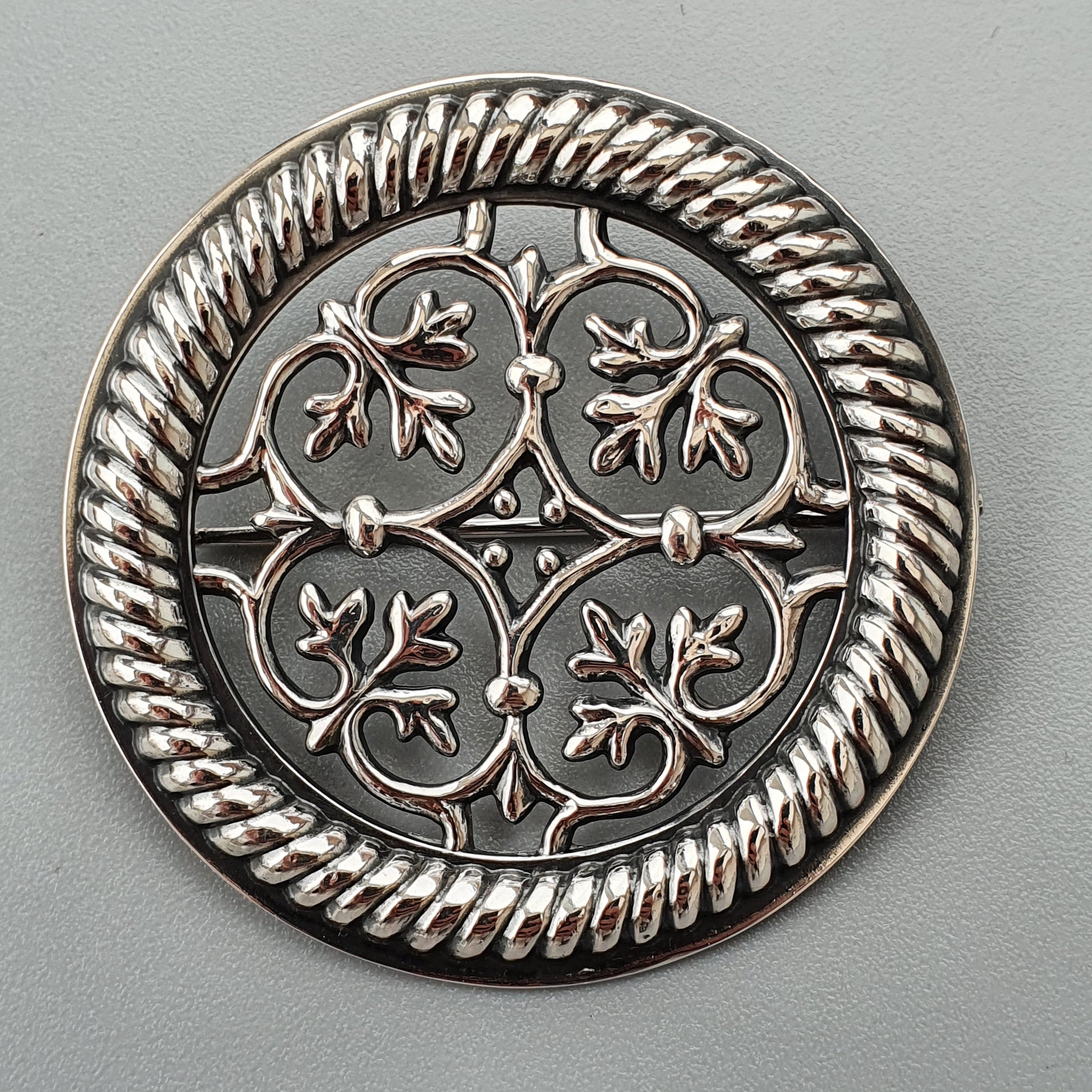 Ornate silver brooch or medallion with intricate floral and rope-twist design.