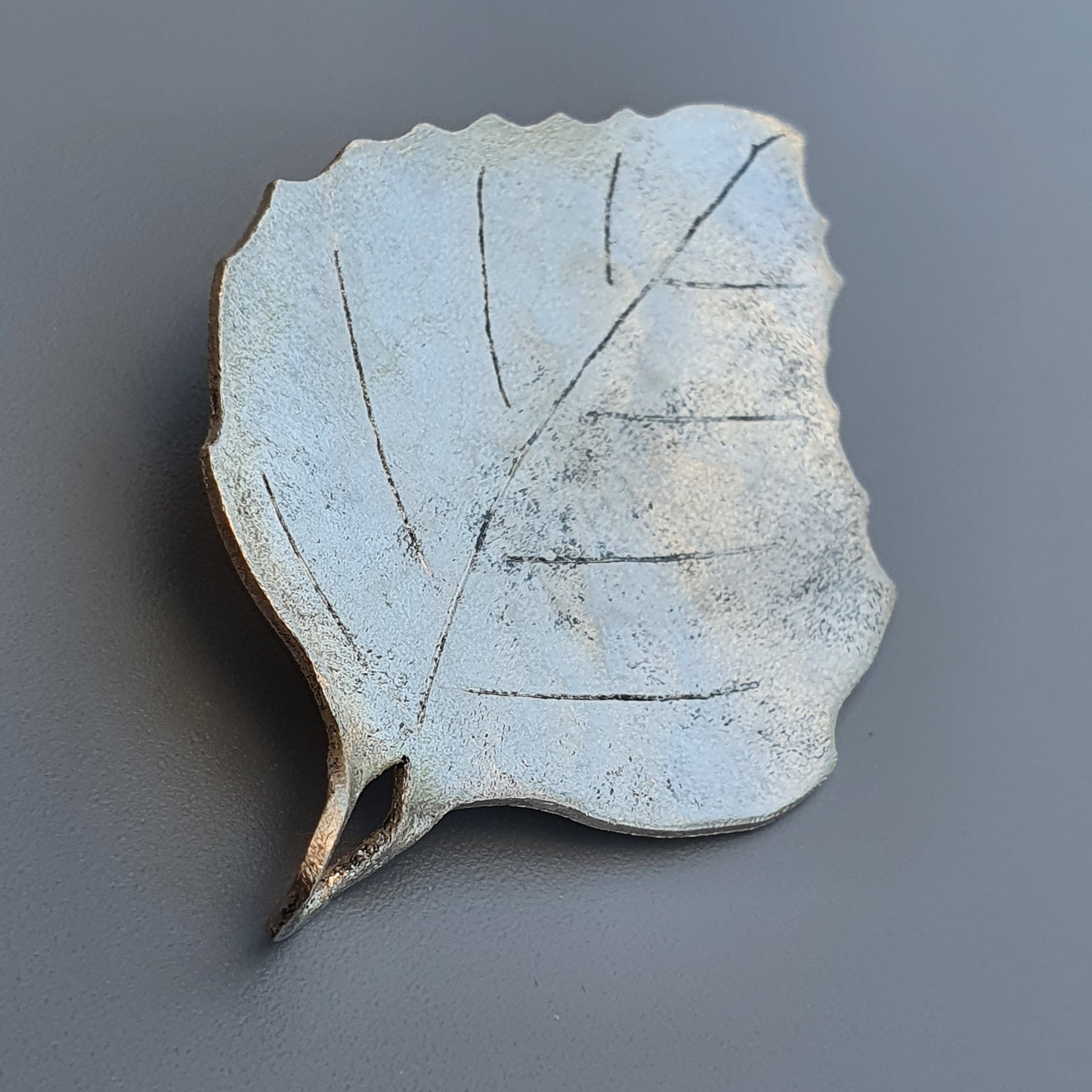 Ceramic or plaster leaf-shaped decorative object with visible veins and a pale blue-gray color.