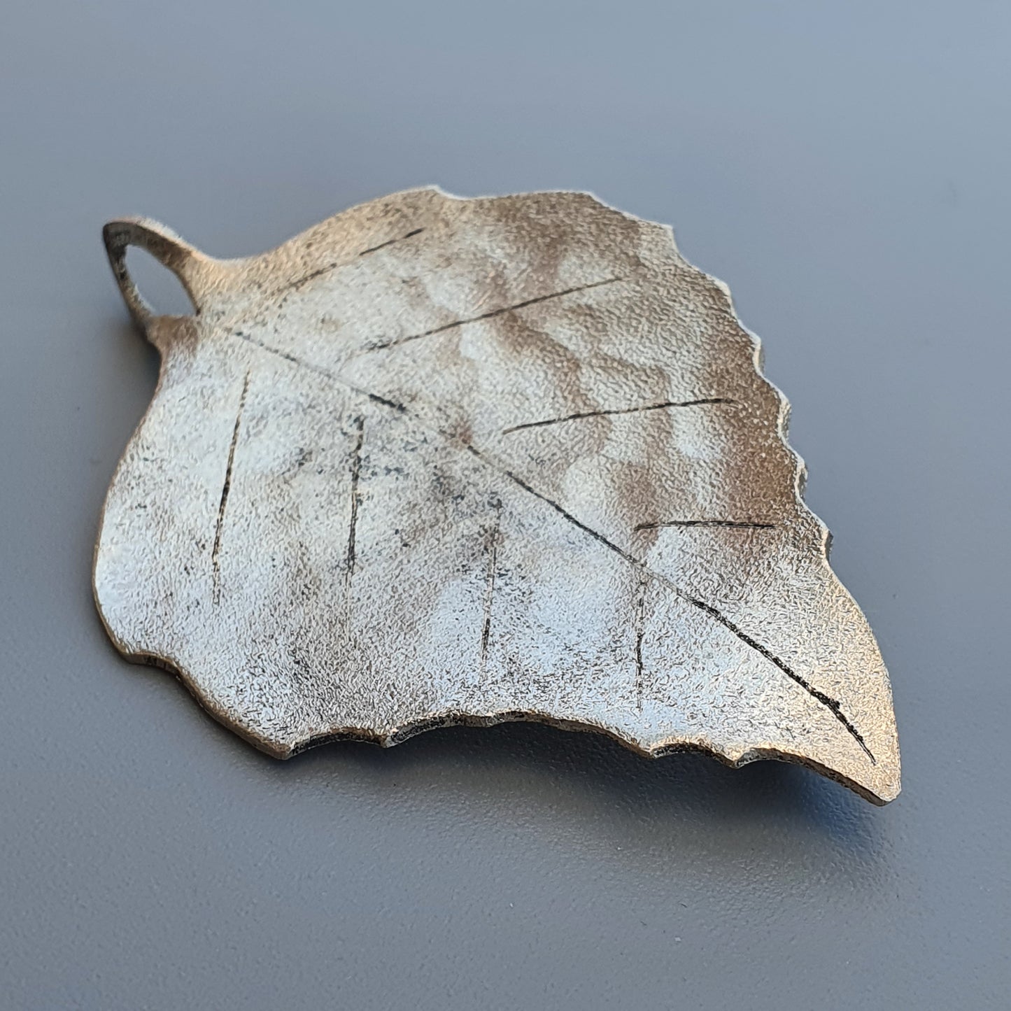 Ceramic leaf-shaped dish or decorative object with veined texture and scalloped edges.