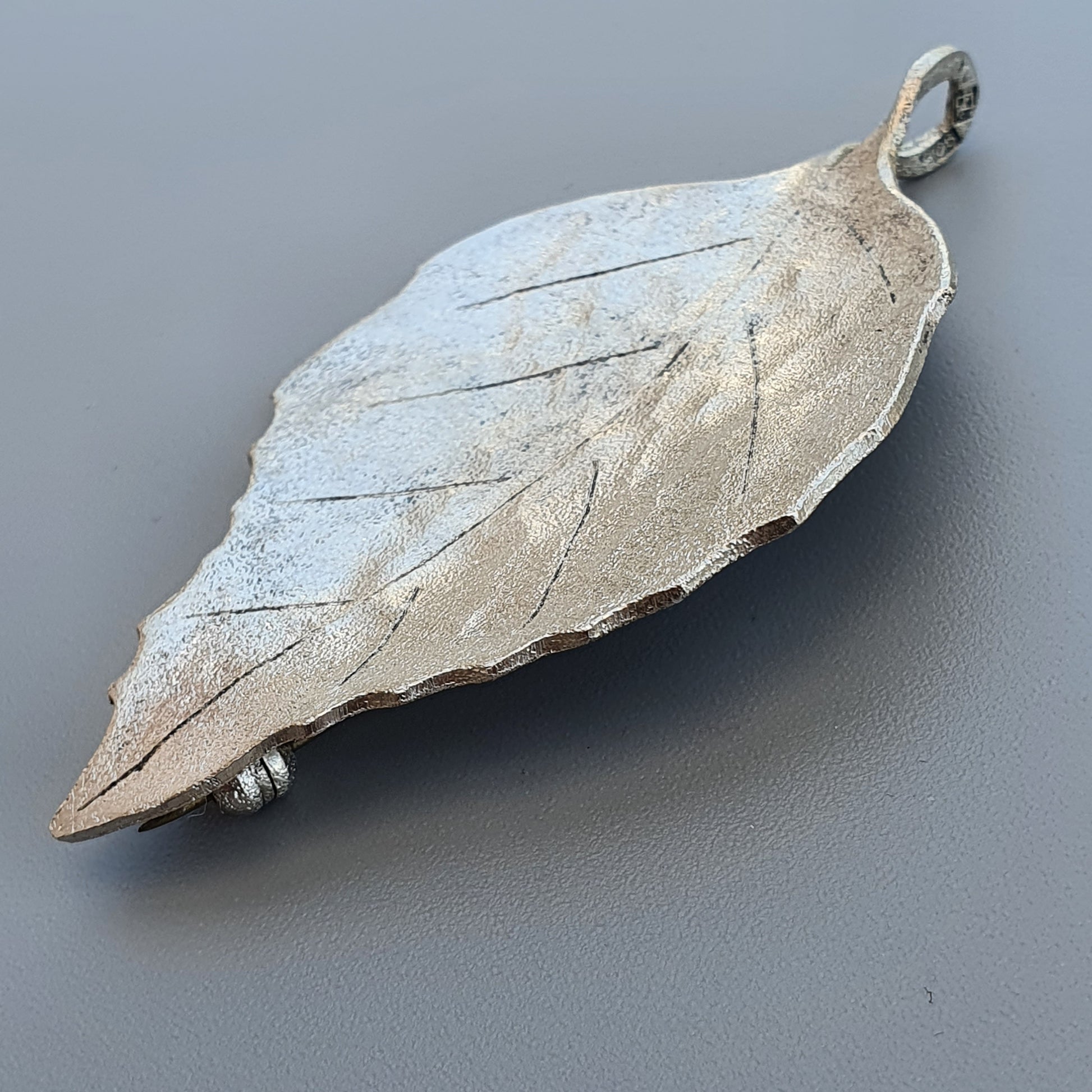 Silver leaf-shaped pendant with detailed vein patterns.