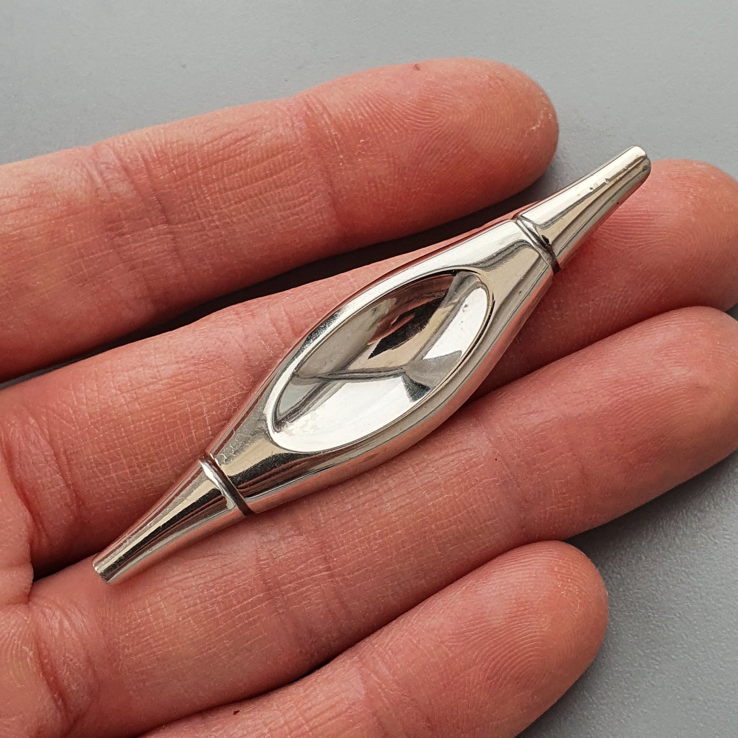 Silver metallic pendant or charm with an eye-like oval shape and pointed ends.