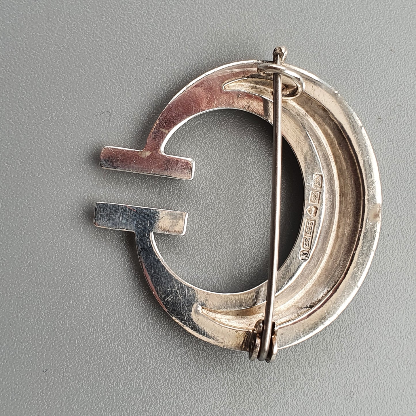 Silver brooch or pin in the shape of a stylized letter G.