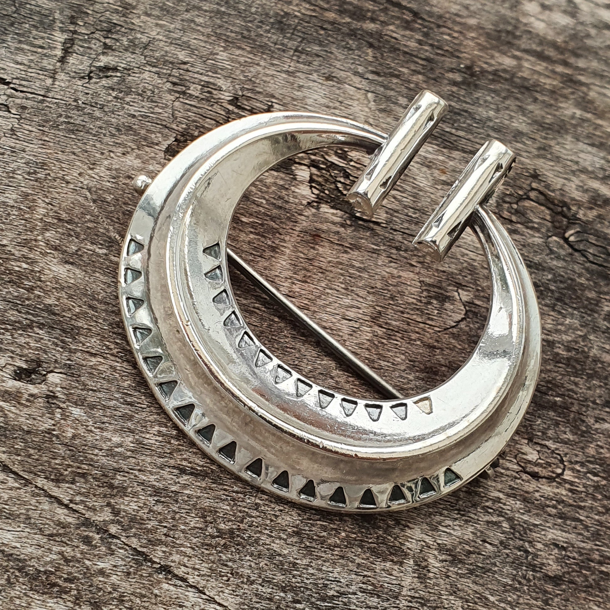 Silver crescent-shaped pendant with decorative notches along its edges.