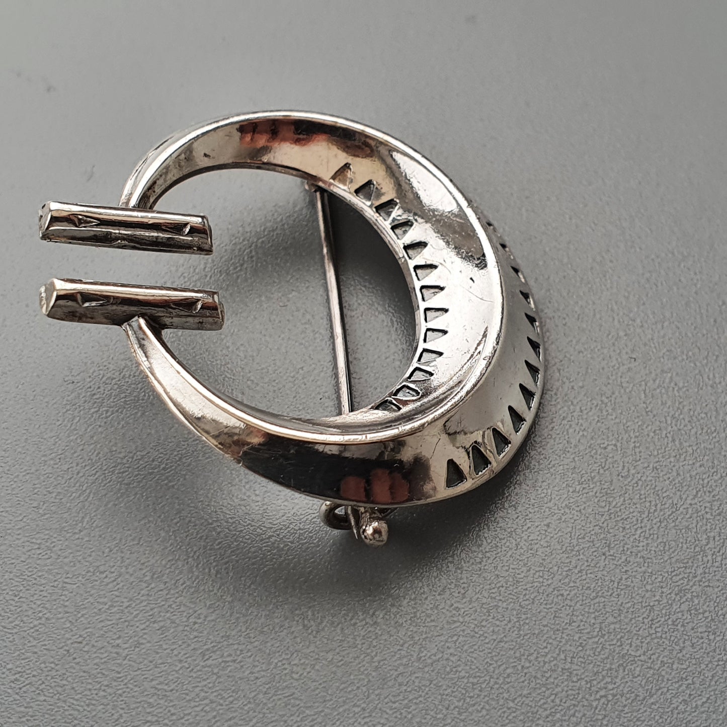 Silver brooch or pin in a crescent shape with decorative etching along the edges.