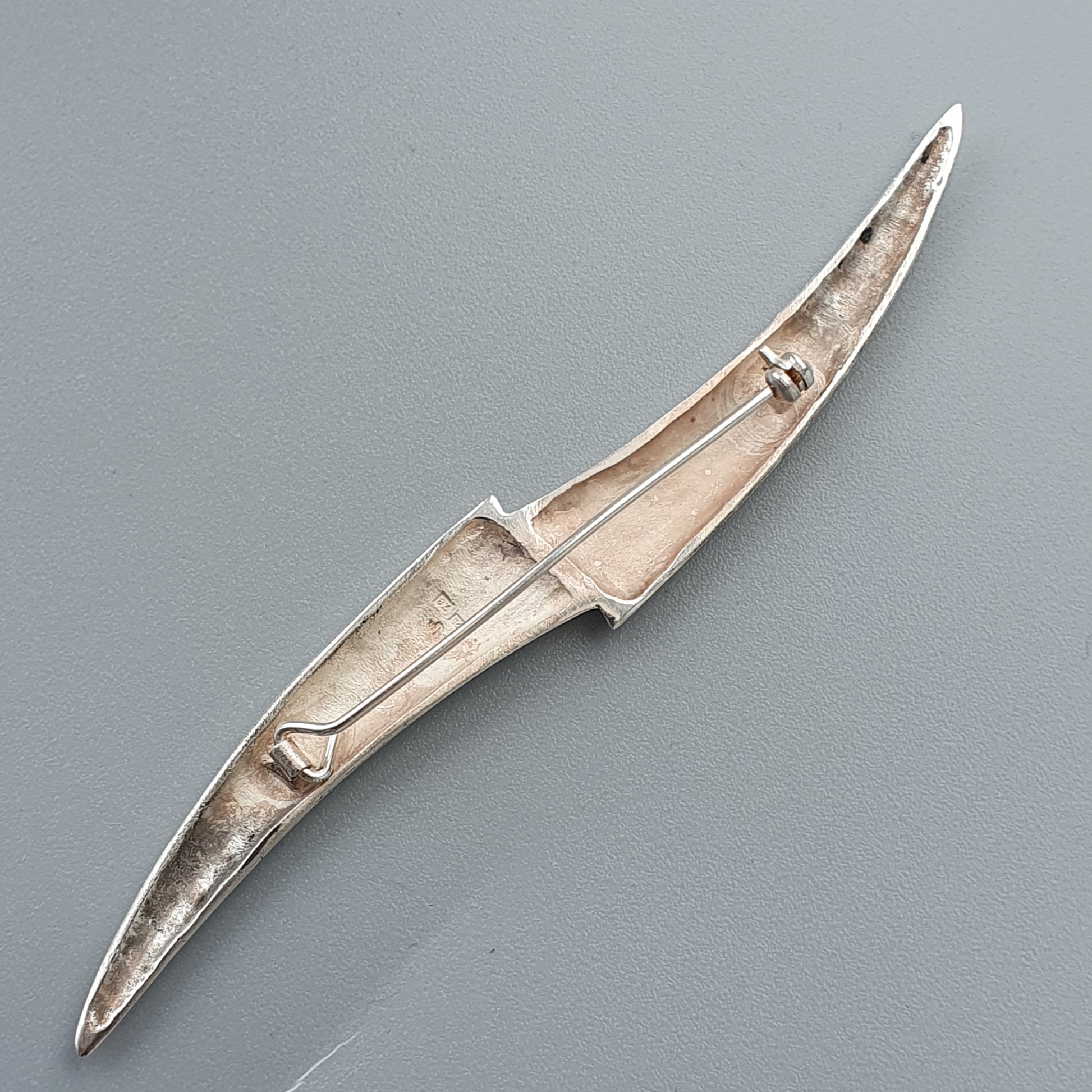 Elongated silver brooch or pin with a curved, tapered shape and minimalist design.