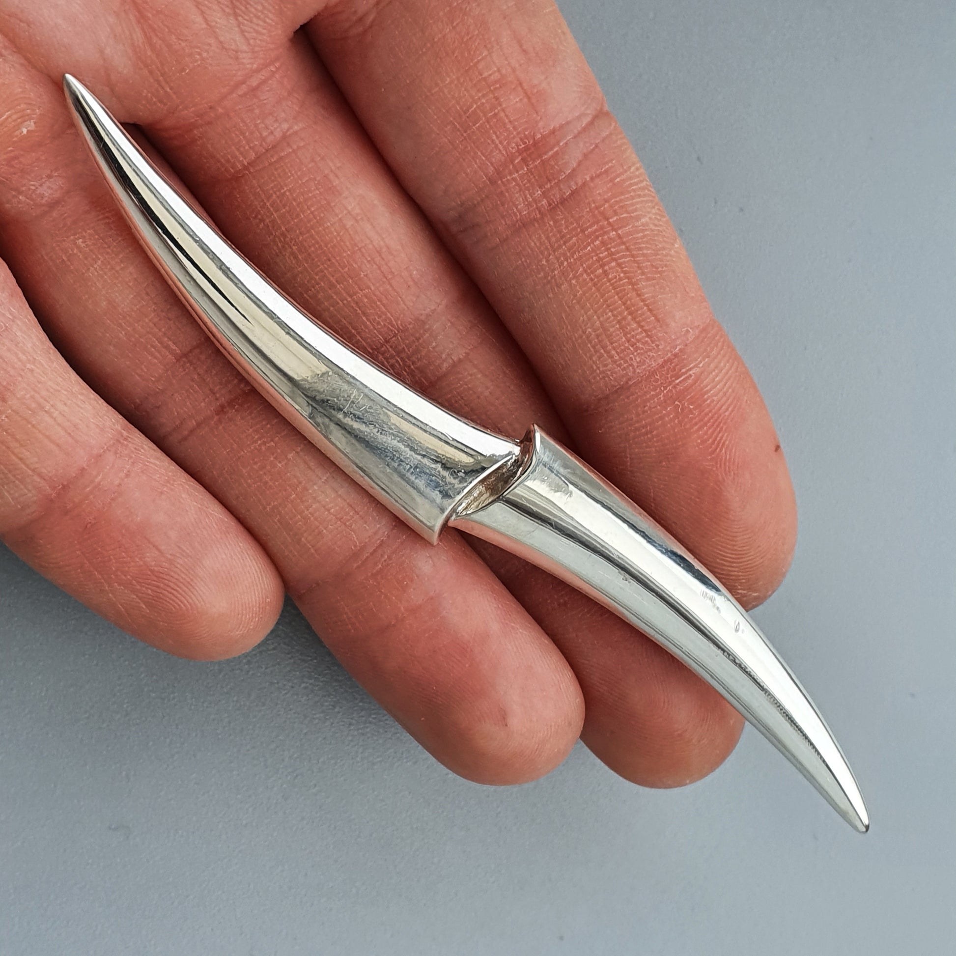 Sleek, curved metal object resembling a stylized double-ended blade or spike.