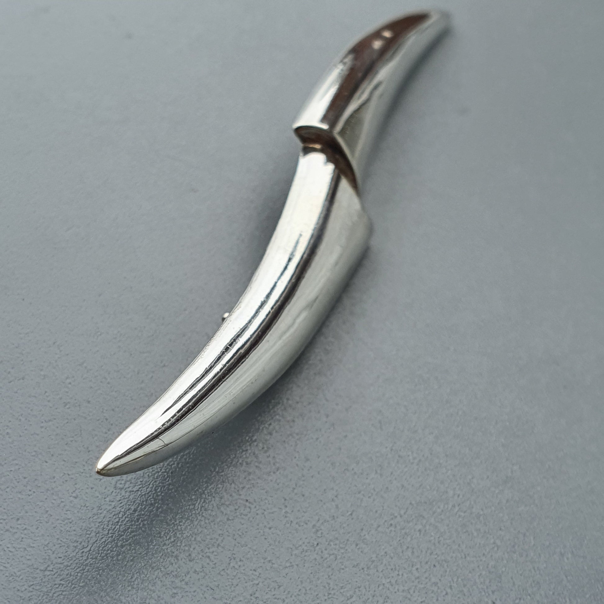 Curved metallic blade or knife with a sleek, polished surface.