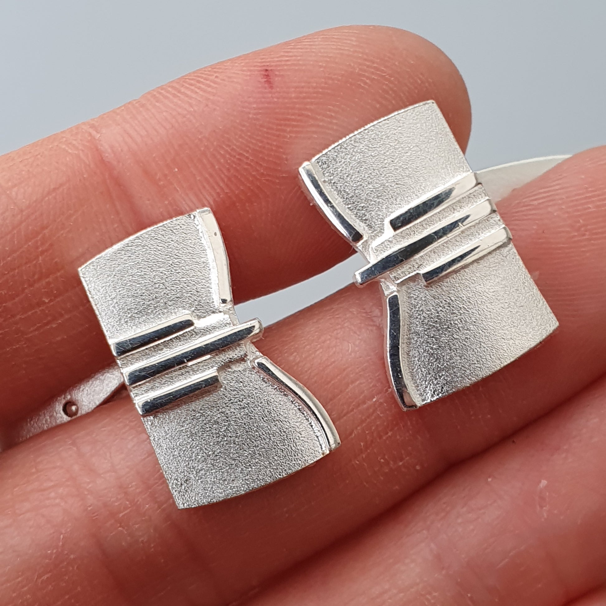 Silver cufflinks with a geometric, modernist design held between fingertips.