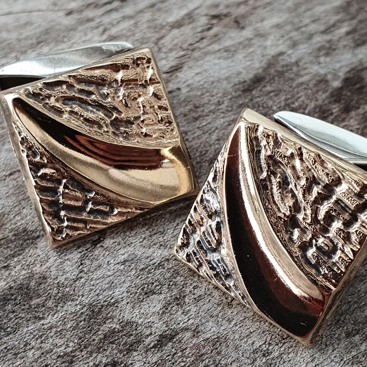 Pair of ornate metallic cufflinks with textured and smooth surfaces.