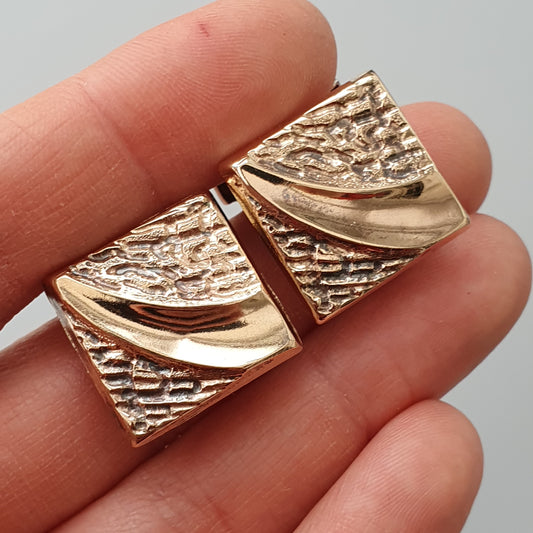 Pair of gold-toned textured rectangular cufflinks with curved smooth accents.