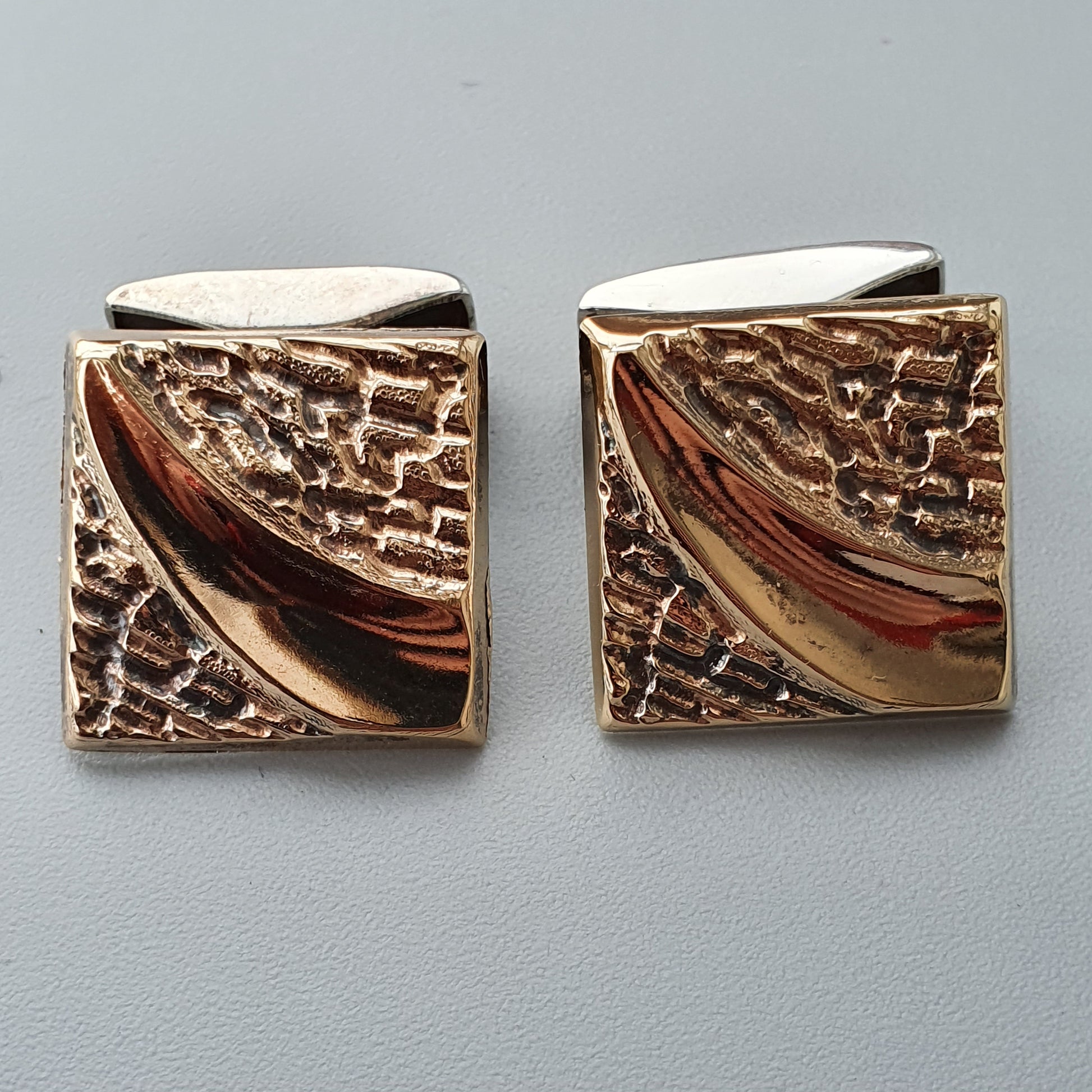 Pair of square gold-toned cufflinks with textured surfaces and smooth diagonal accents.