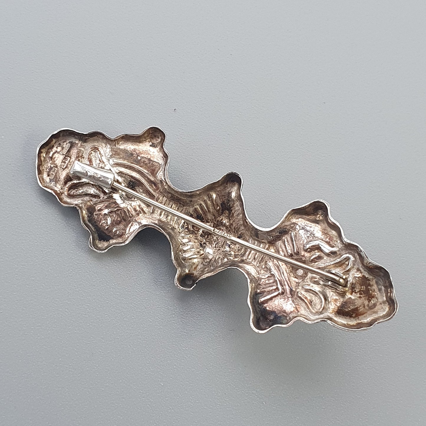 Metallic oak leaf-shaped brooch or pin with textured surface and irregular edges.