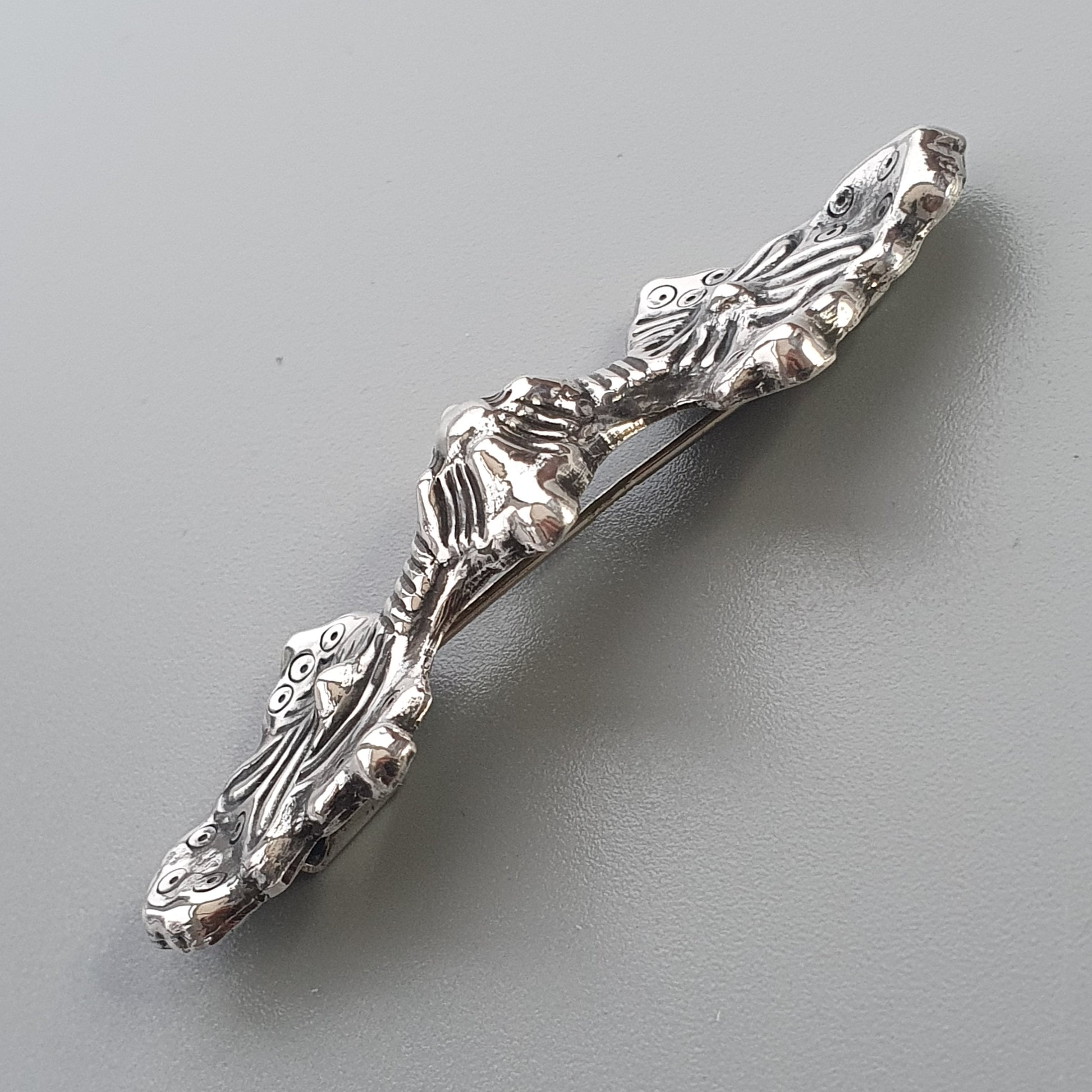 Silver-colored metal pin or brooch shaped like a lizard or salamander with intricate skeletal detailing.