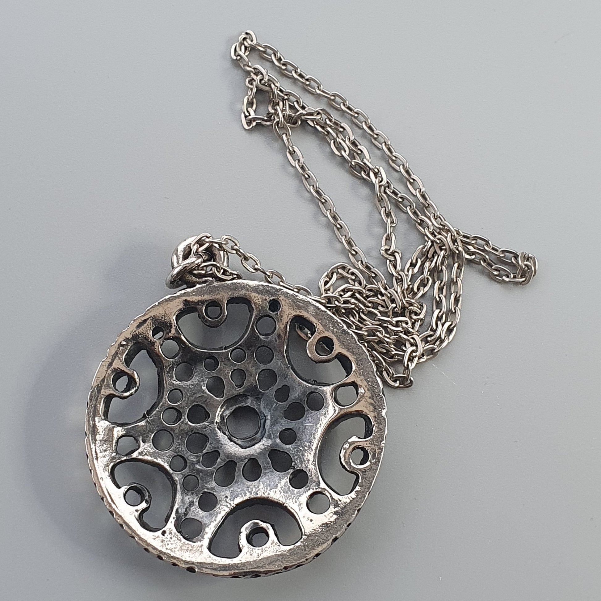 Circular silver pendant with an intricate cutout pattern on a chain necklace.