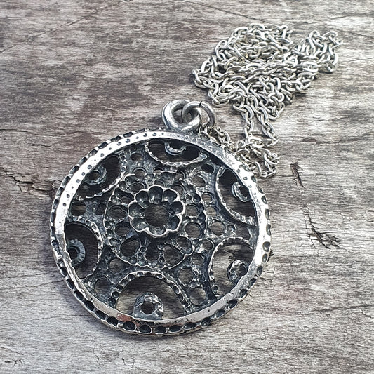 Ornate circular pendant with intricate floral design on a silver chain.